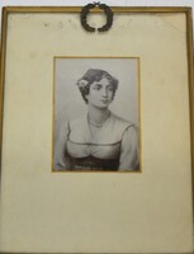Ασπρόμαυρη φωτογραφία που εικονίζει την Μαντώ Μαυρογένους. Το κάδρο φέρει και δάφνικό μεταλλικό στεφάνι.