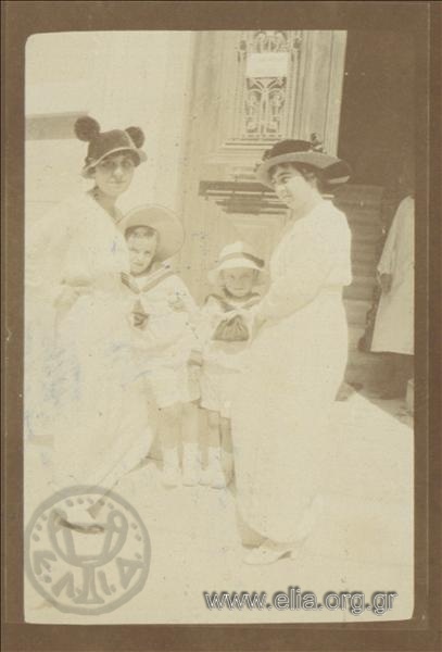 Δύο γυναίκες με δύο παιδιά μπροστά σε είσοδο.