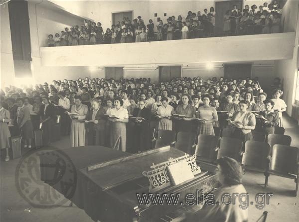 Female students and professors singing at a morning gathering.