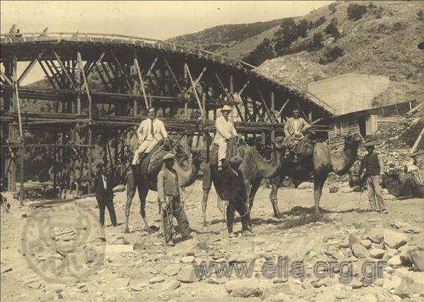 The construction of the bridge at Nestos river. The contractors (?) pose  on camels in the riverbed, with the bridge as a background.