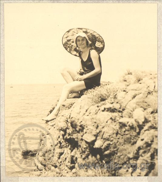 Woman in a swimsuit and umbrella on a rock above the sea