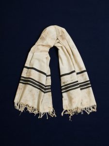 Prayer shawl, white cotton with black stripes along the edge, white square corner reinforcements.