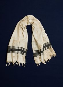 Prayer shawl, white cotton with black stripes along the edge, white square corner reinforcements.