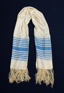 Prayer shawl, cream silk with blue stripes along the edge, cream square corner reonforcements.