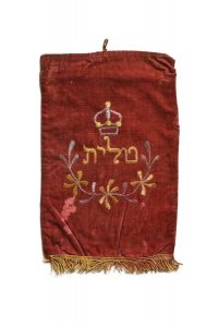 Drawstring bag for prayer shawl, dark red velvet with light yellow and lavender embroidery, inscribed with 'Tallit'.