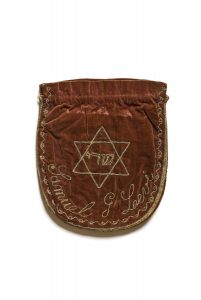 Drawstring bag for prayer shawl, maroon brown velvet embroidered with fine plaited strands, front side with central motif of the Star of David inscribed with 'Shaddai', below owner's name Samuel G